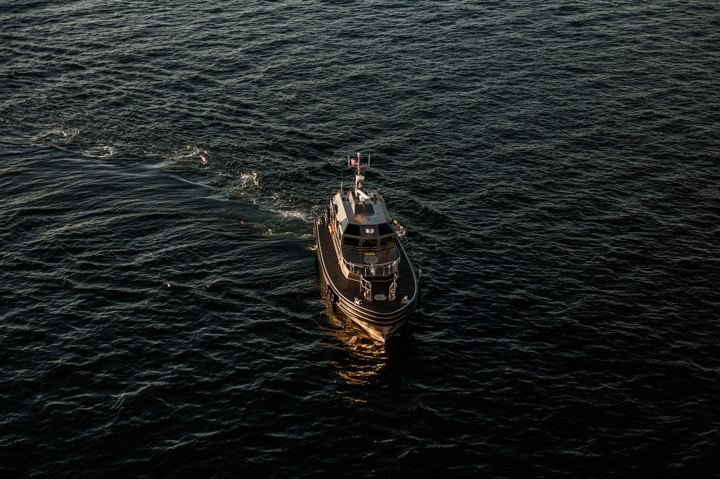 A small fishing boat seen from high above, running alone across dark rippled water with its wake curling away behind it.
