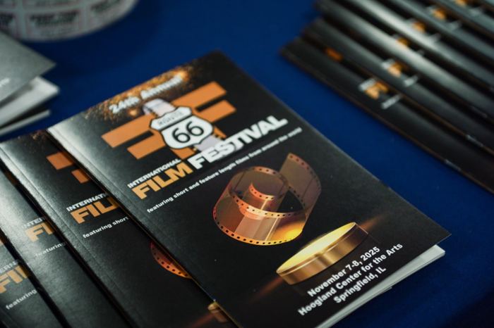 A stack of programs for the 24th annual International Route 66 Film Festival fanned across a table, the cover showing a gold film reel and the dates at the Hoogland Center for the Arts in Springfield.